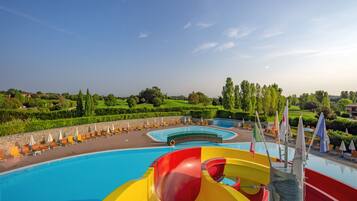 A swimming pool with a water slide, lounge chairs, and flags.