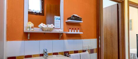 Een badkamer met een wit wastafel, een spiegel en oranje wanden. Er staan toiletartikelen op een plank en een handdoek hangt aan de muur.