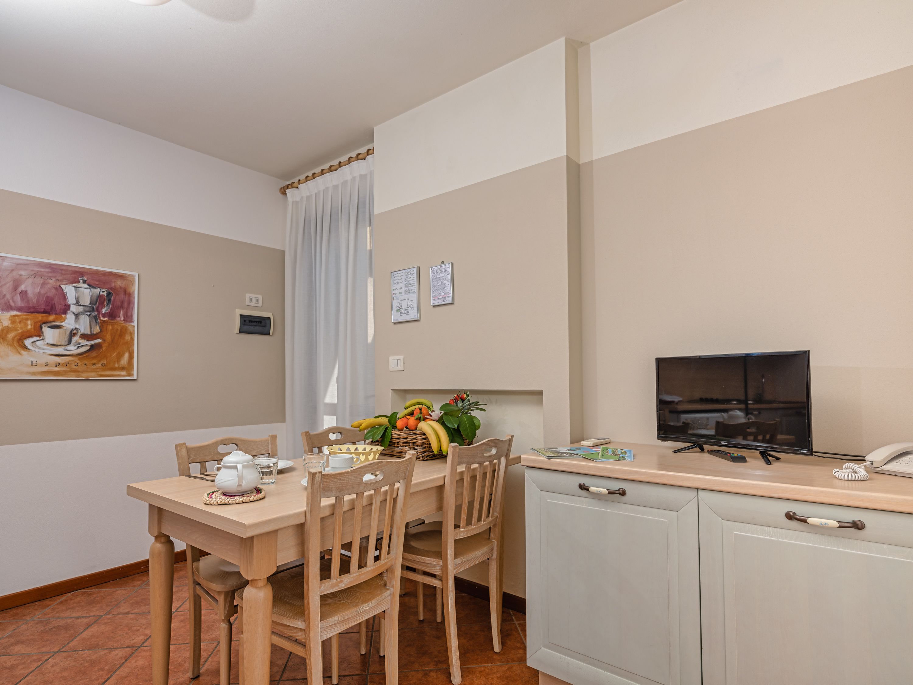 A dining area with a wooden table, chairs, a television, and a kitchen counter.
