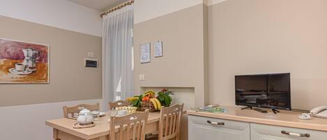 A dining area with a wooden table, chairs, a television, and a kitchen counter.