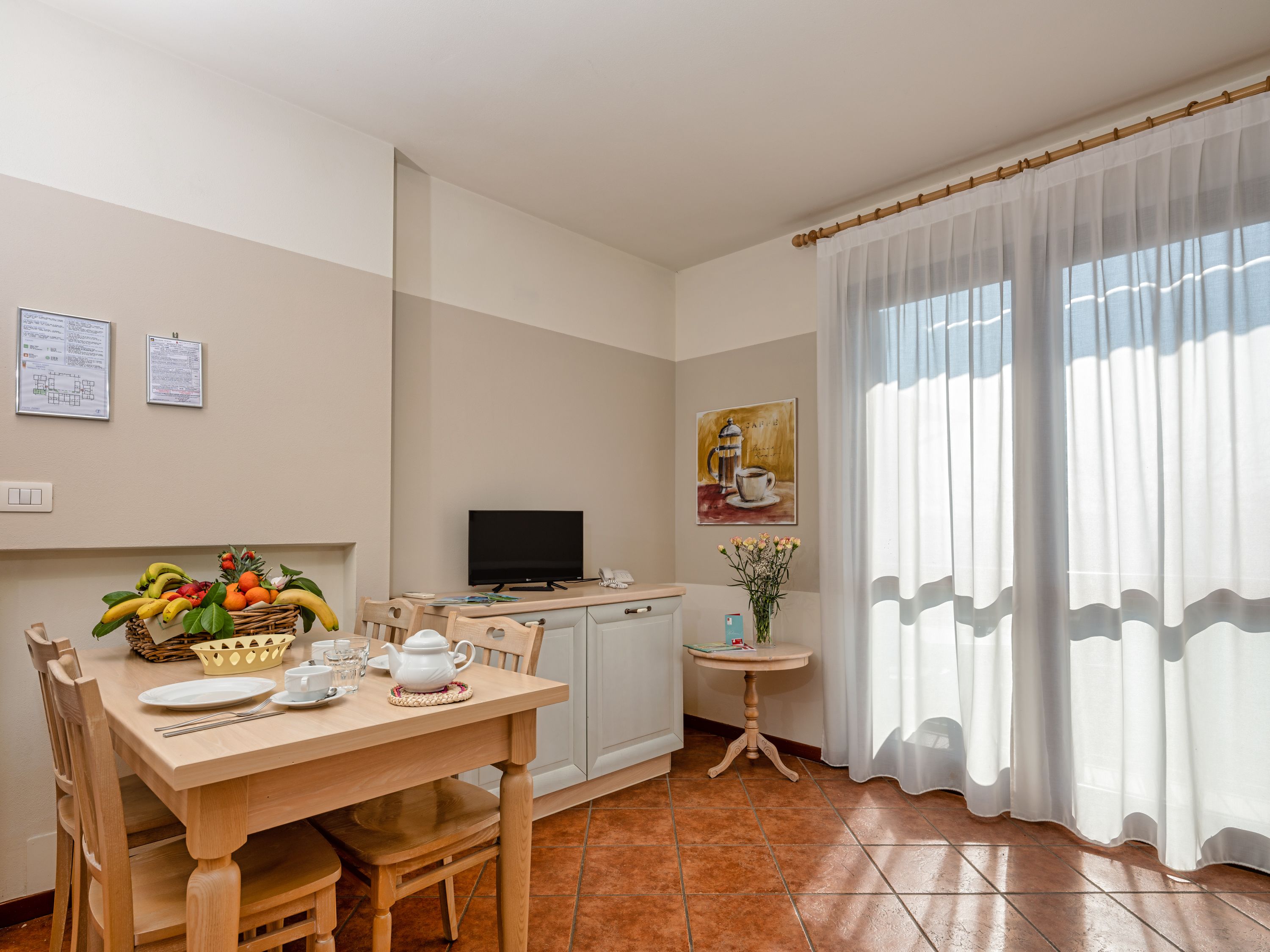 Un comedor con una mesa de madera dispuesta para dos personas, un televisor y un cuadro en la pared.