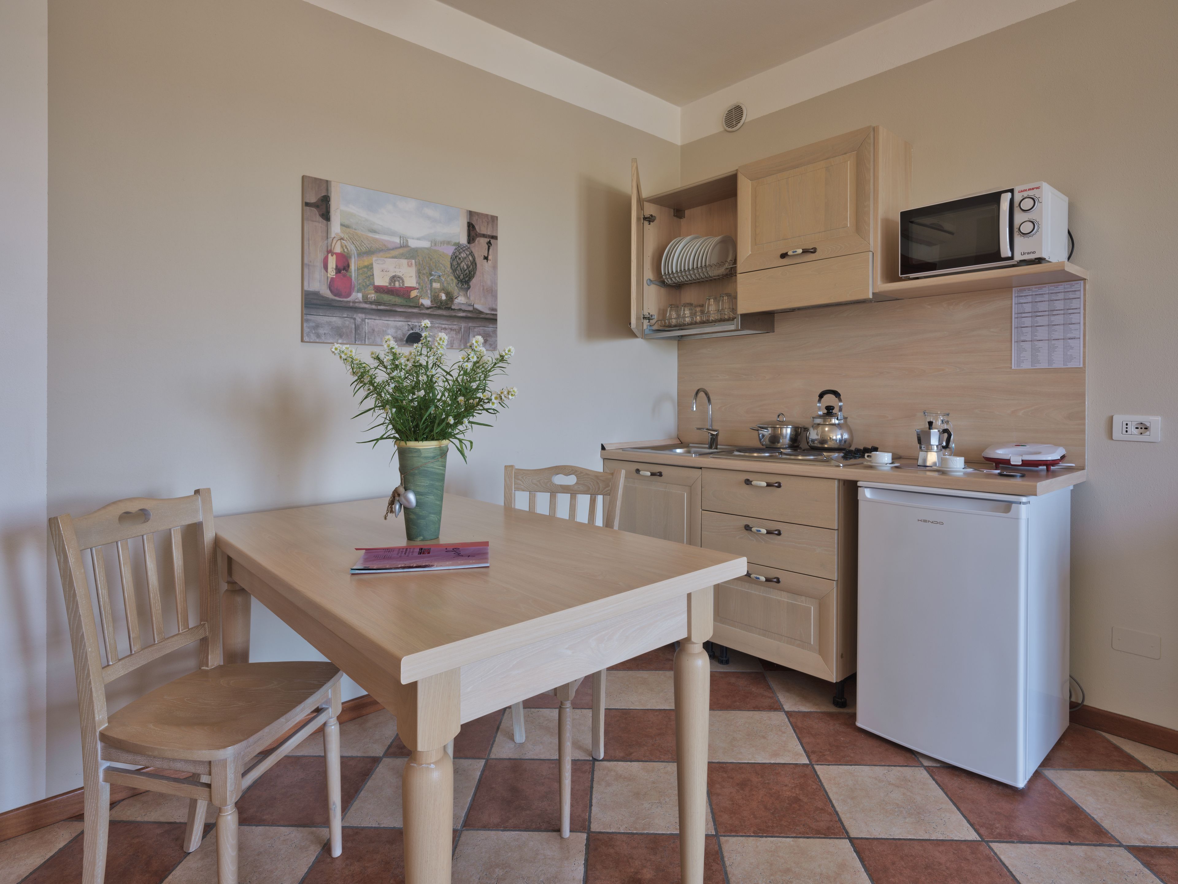 Cocina compacta con una mesa de comedor, sillas, un refrigerador pequeño y un microondas.