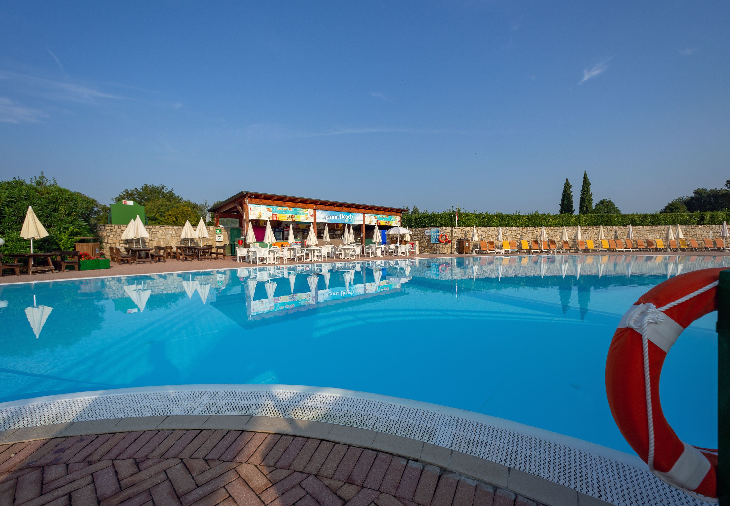Ein Swimmingpool mit Liegestühlen und Sonnenschirmen, einem Rettungsring und einem Gebäude mit Außenbereich.