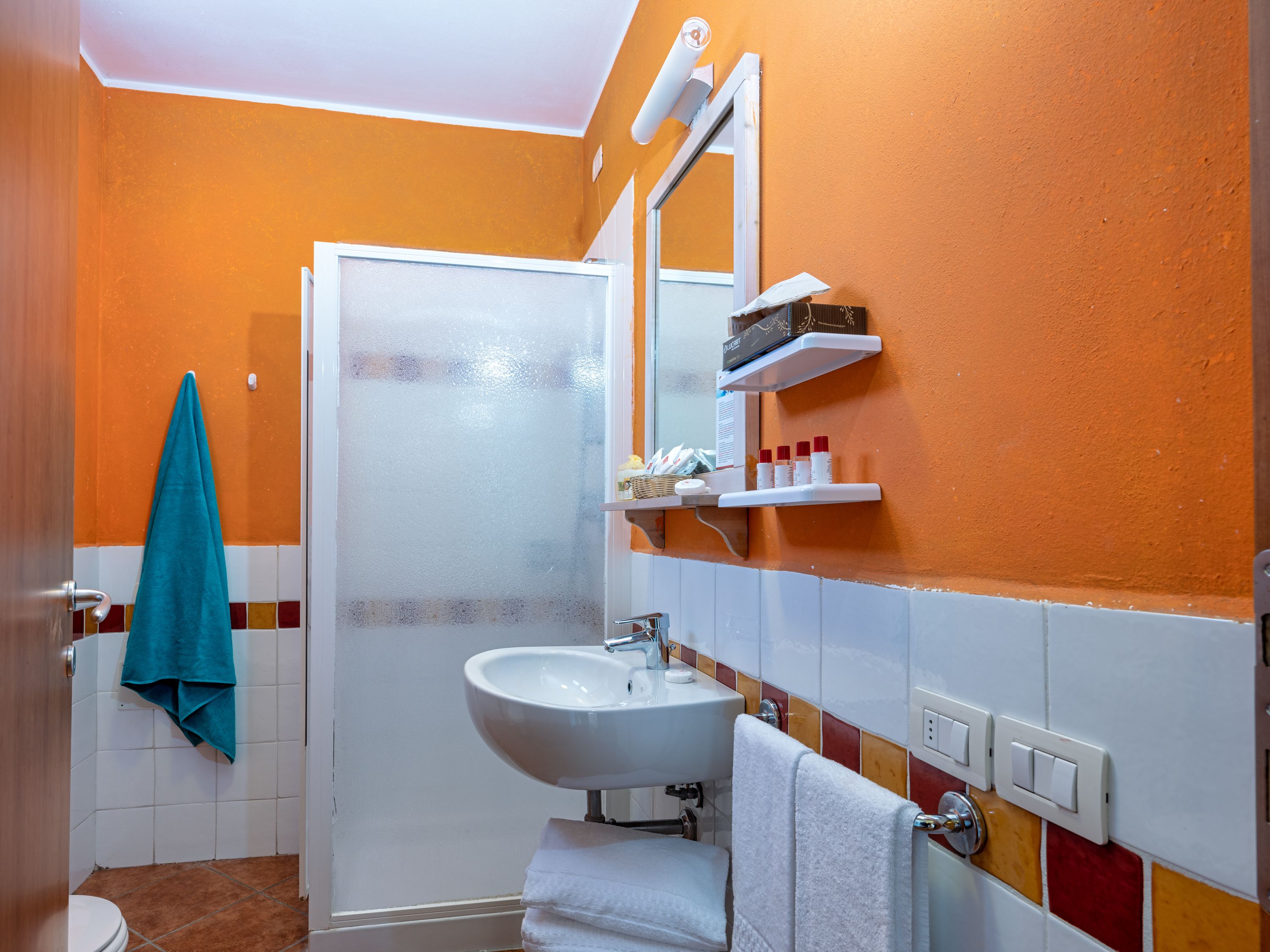 Un baño con un lavamanos blanco, un espejo y una repisa con artículos de aseo.