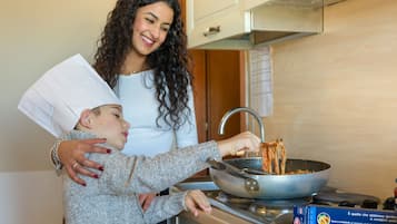 Une personne prépare des spaghettis dans une cuisine équipée d’une cuisinière et d’une poêle.
