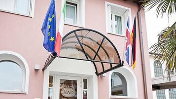 A building with a pink facade, a glass entrance, and flags of the EU, UK, and Germany.