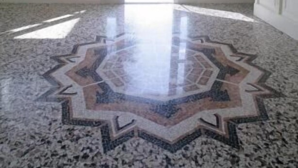 Un vestíbulo amplio con una gran araña ornamentada, un suelo estampado y vistas al exterior a través de la puerta.