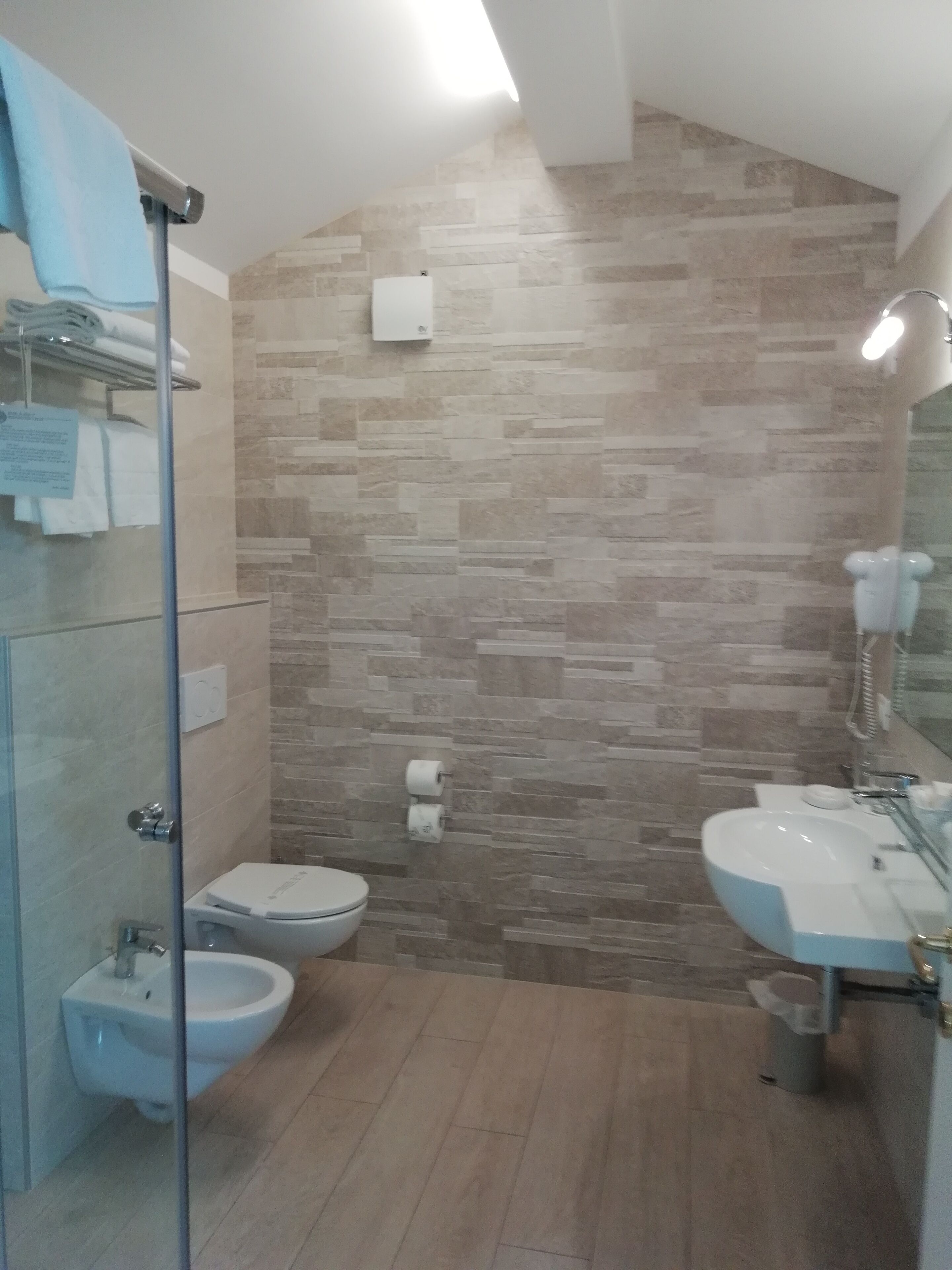 Une salle de bain avec un mur en pierre, un bidet, des toilettes et un lavabo avec un miroir.