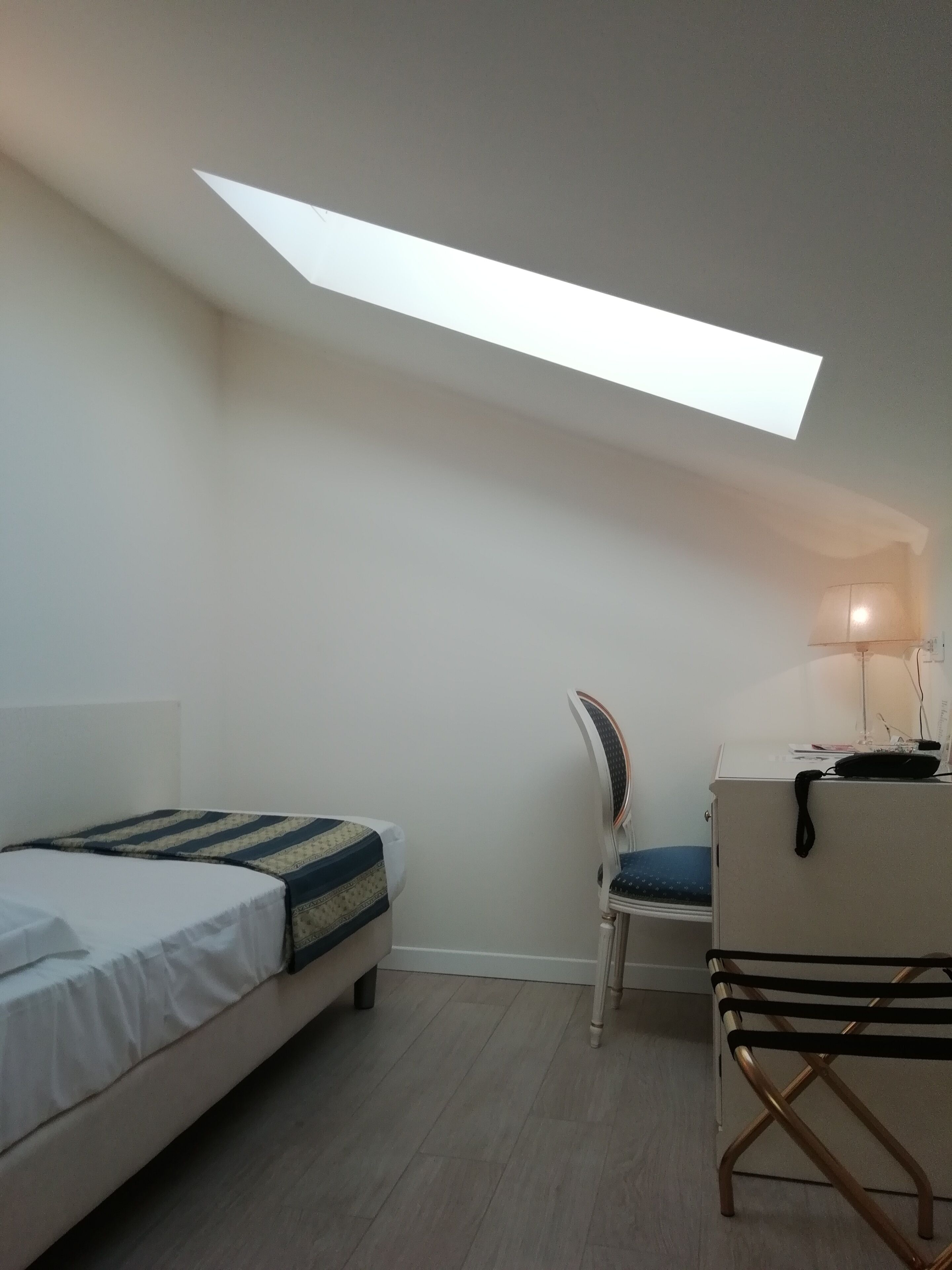A bedroom with a bed, a desk, a chair, and a skylight.