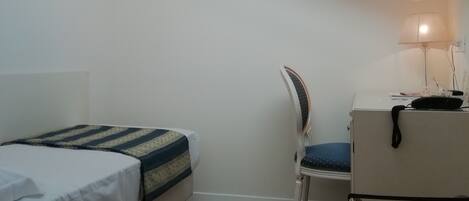 A bedroom with a bed, a desk, a chair, and a skylight.