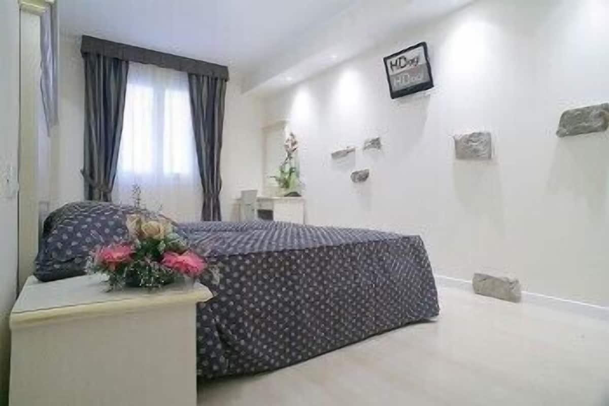 Ein Schlafzimmer mit einem Bett, einem Nachttisch mit Blumenvase, einer Kommode und einem an der Wand befestigten Schild.