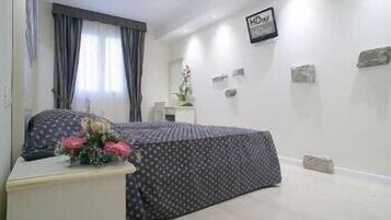 Une chambre à coucher avec un lit, une table de chevet ornée d’un vase de fleurs, une commode et un panneau décoratif fixé au mur.