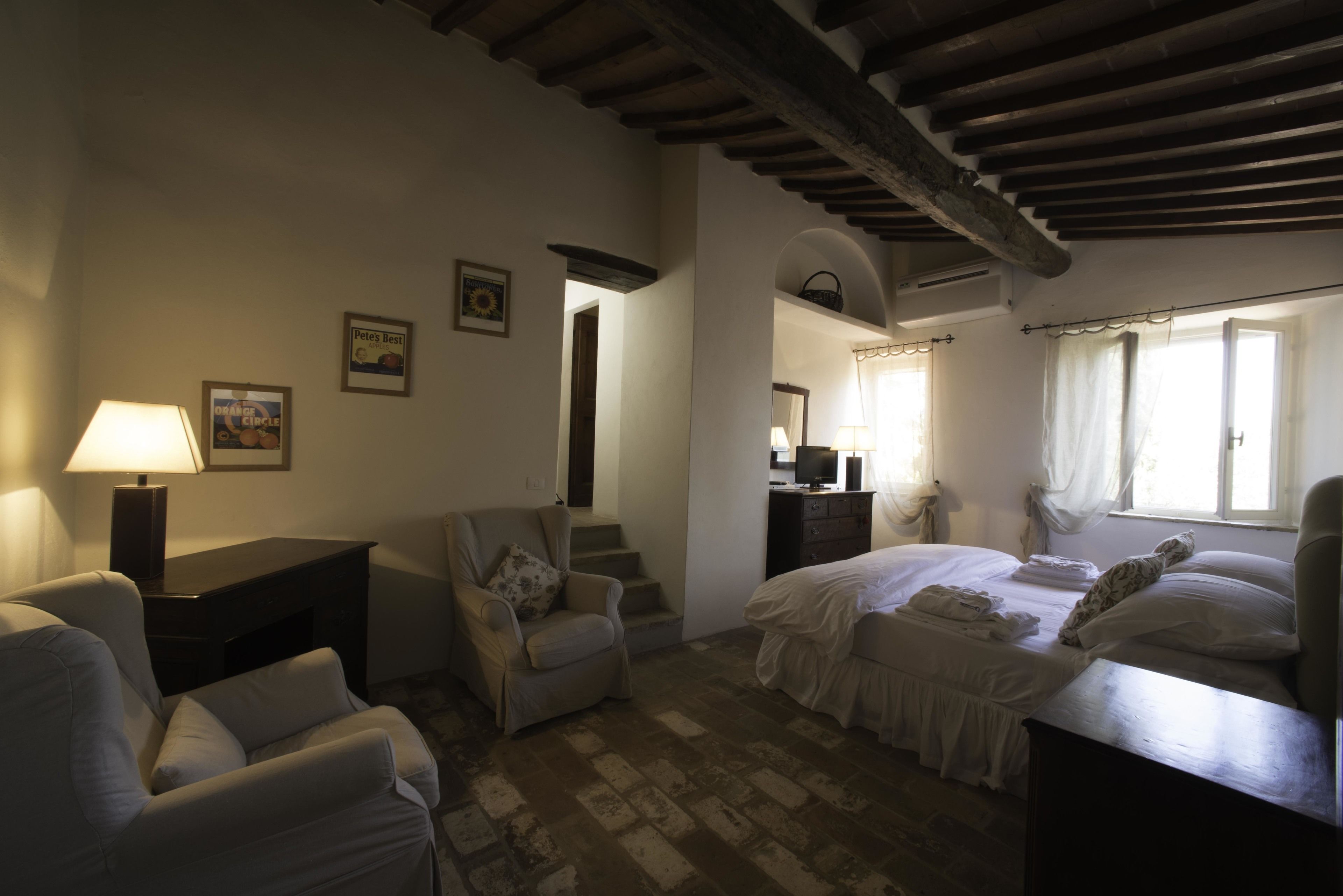A bedroom with a bed, a chair, a desk, and a lamp. There is a staircase leading to another room.