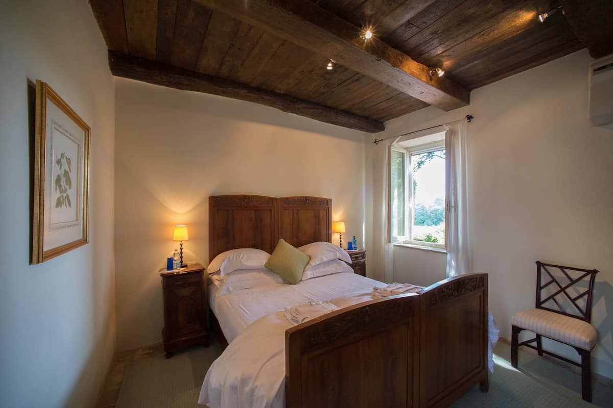 A bedroom with a wooden bed, bedside lamps, a chair, and a window with curtains.