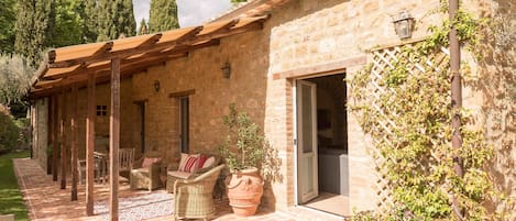A stone building with a covered patio, wicker furniture, and potted plants.
