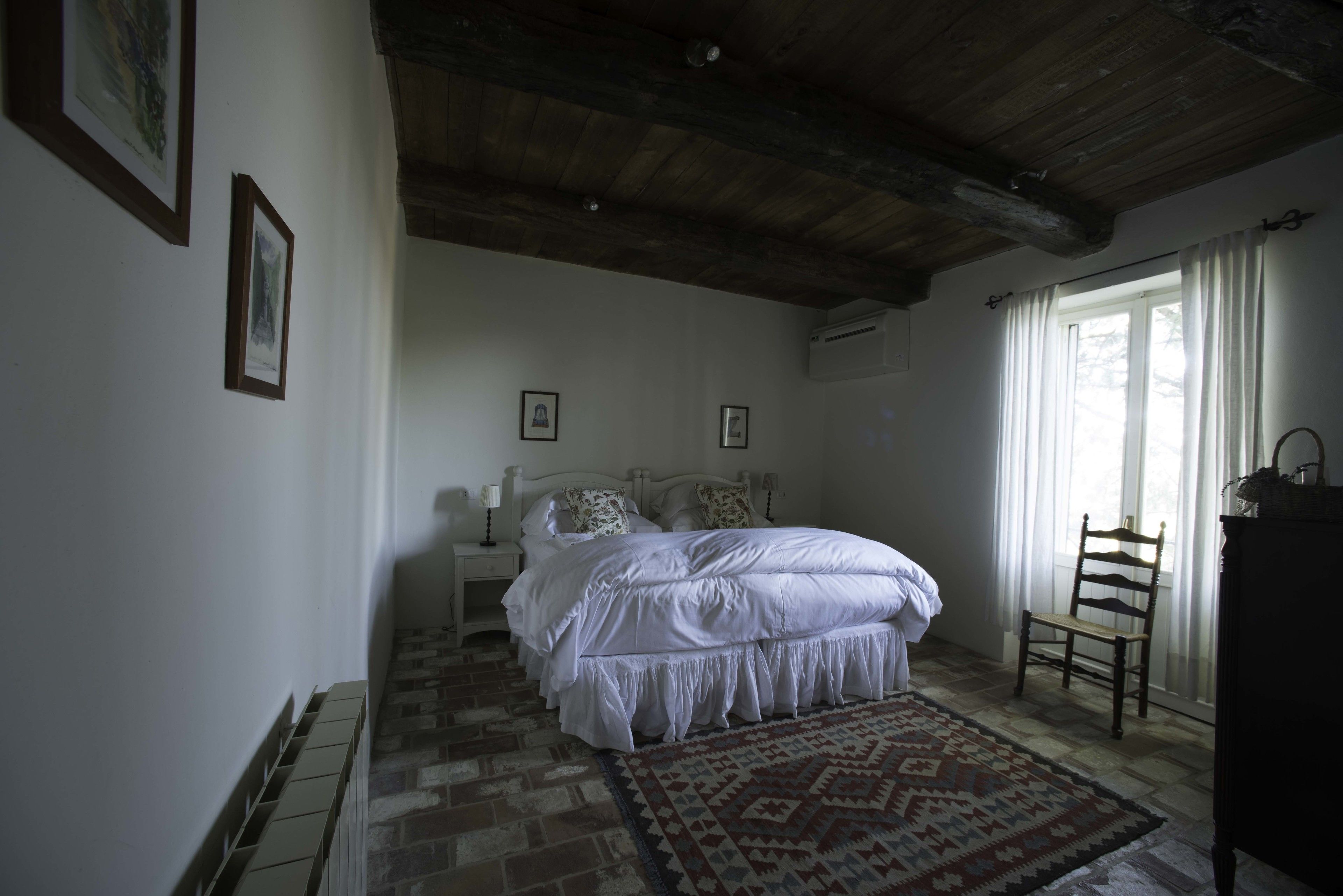 Une chambre avec un grand lit, un plafond en bois, un tapis à motifs et une chaise près de la fenêtre.