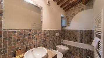 Une salle de bain dotée d’un grand lavabo, de toilettes et d’une baignoire, avec des murs recouverts de mosaïques et des poutres en bois.