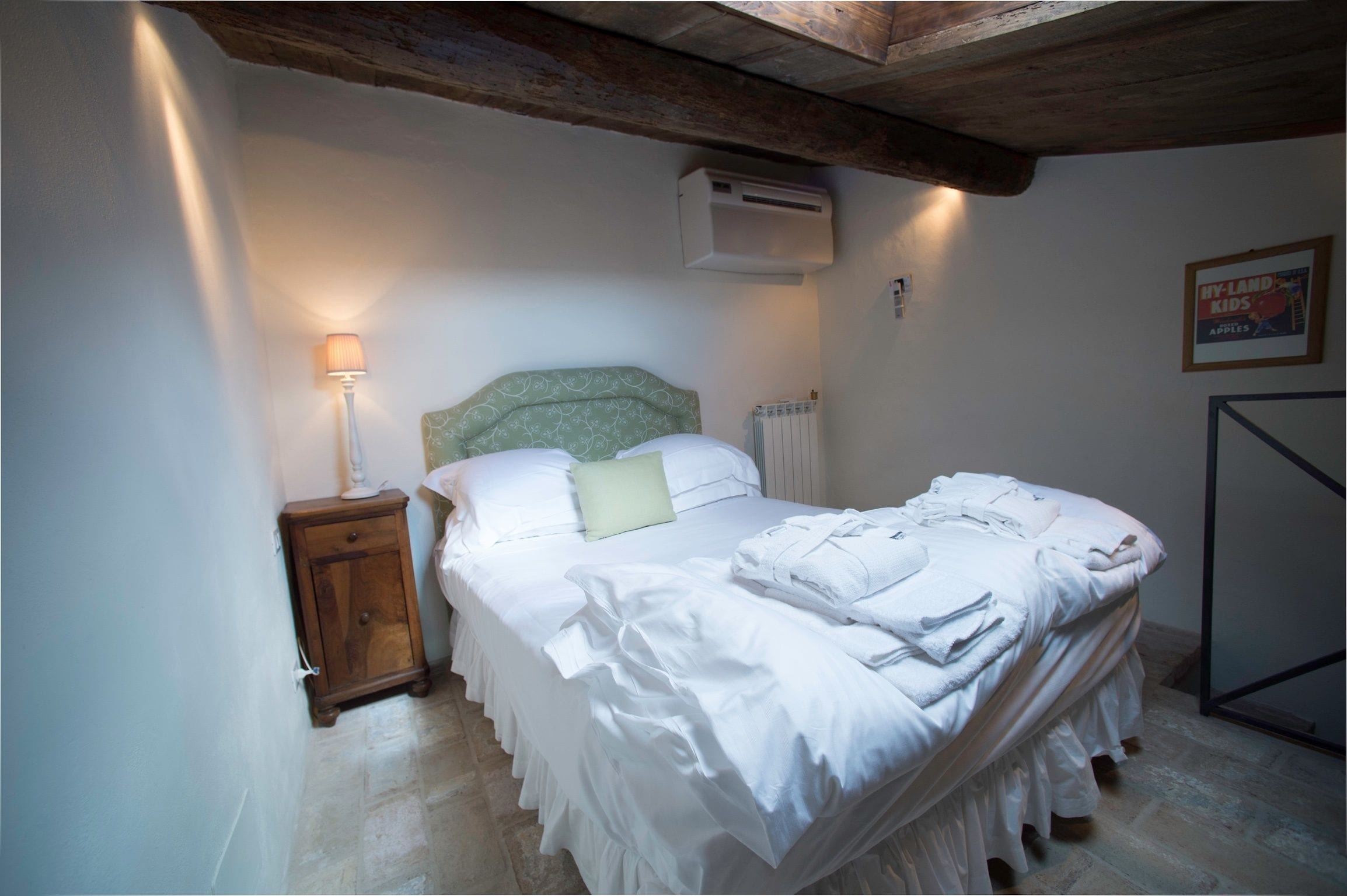 A neatly made bed with white linens, a bedside lamp, and a radiator.