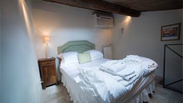 A neatly made bed with white linens, a bedside lamp, and a radiator.