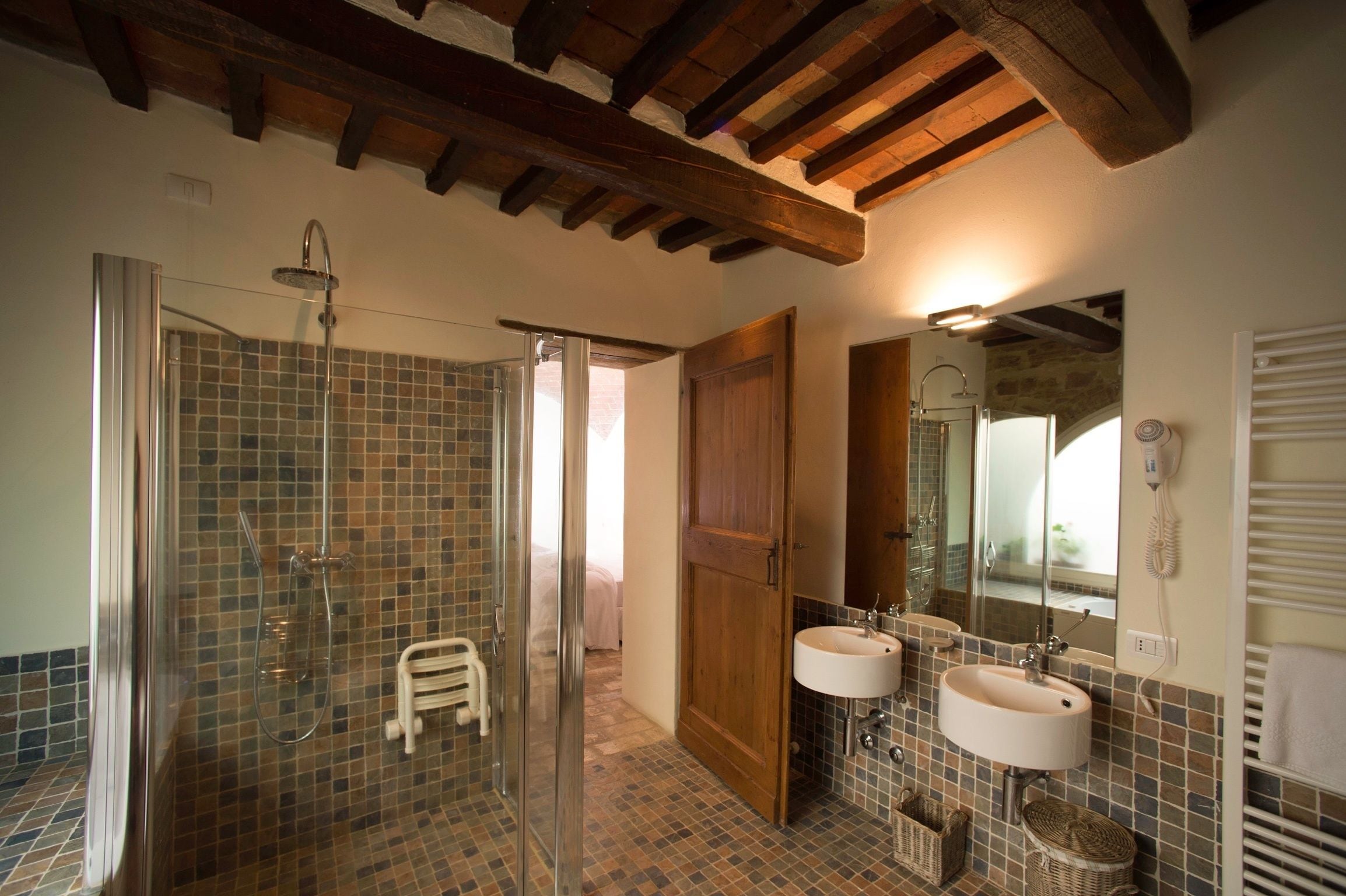 Un baño con cabina de ducha de vidrio, dos lavamanos, una puerta de madera y un espejo.