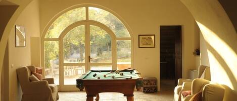 A cozy room with a pool table, comfortable seating, and a large arched window offering a view of the outdoors.