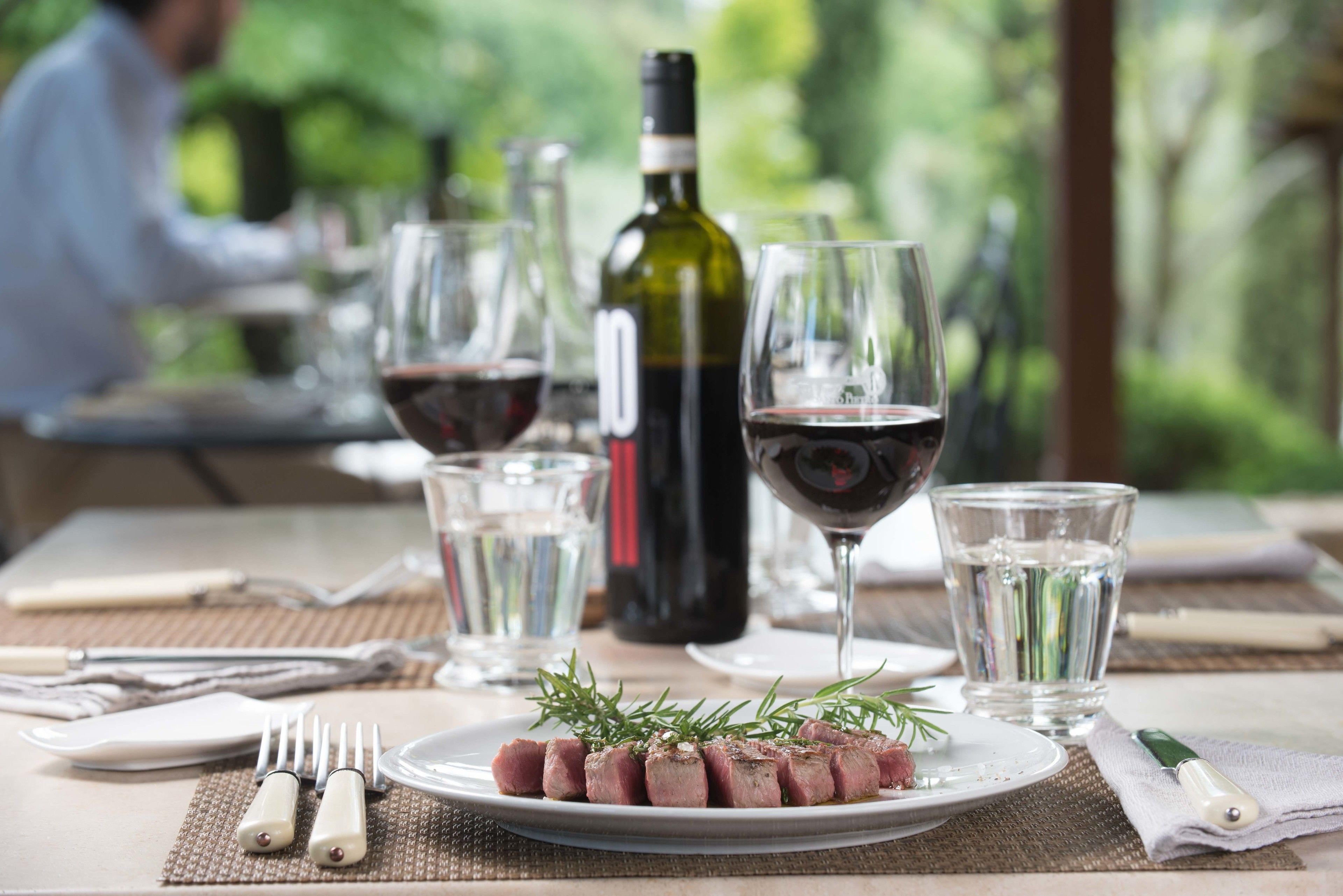 Une table à manger avec une assiette de nourriture, des verres à vin et des bouteilles.