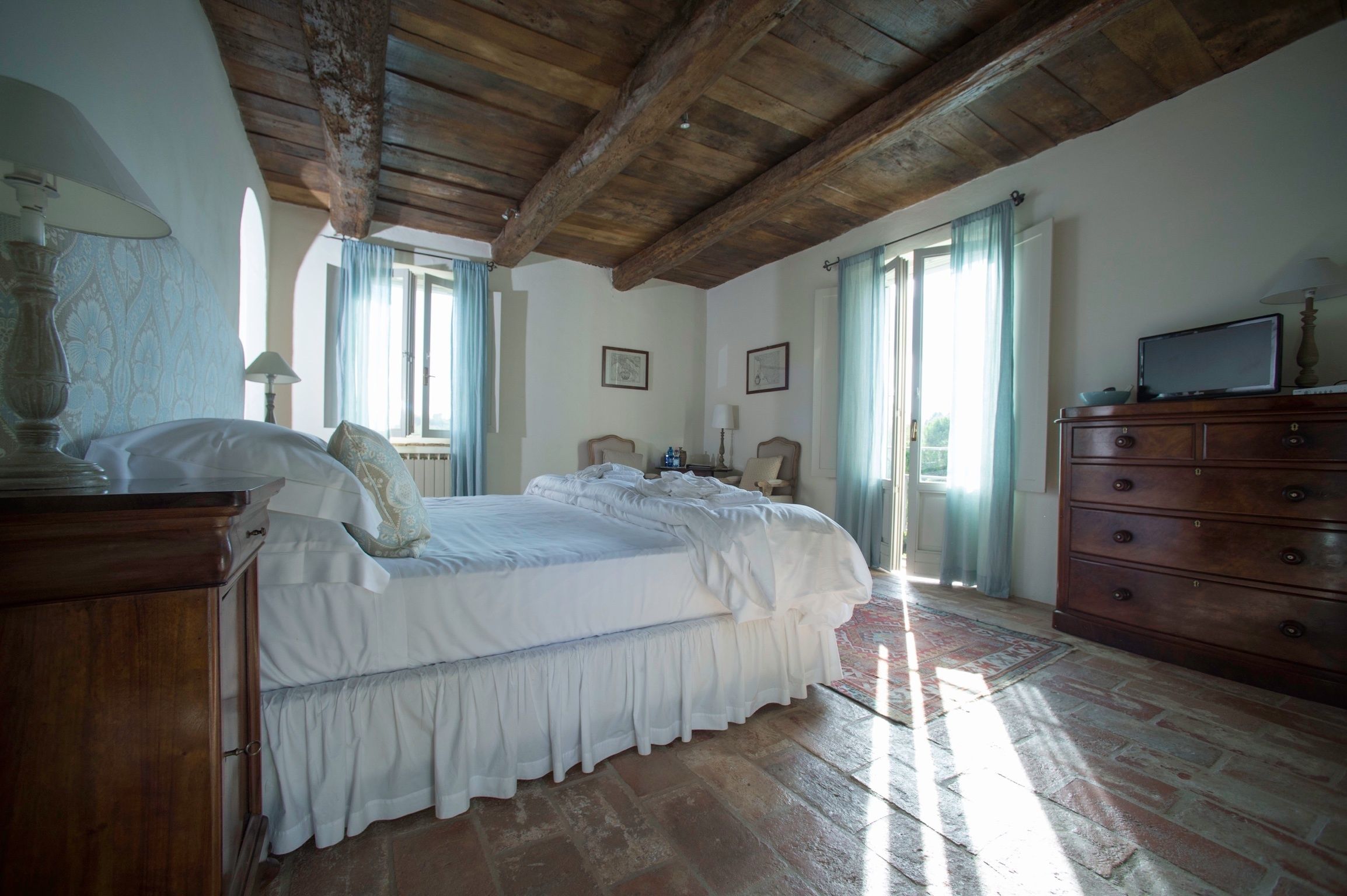 A bedroom with a large bed, wooden ceiling beams, a dresser, and a television.