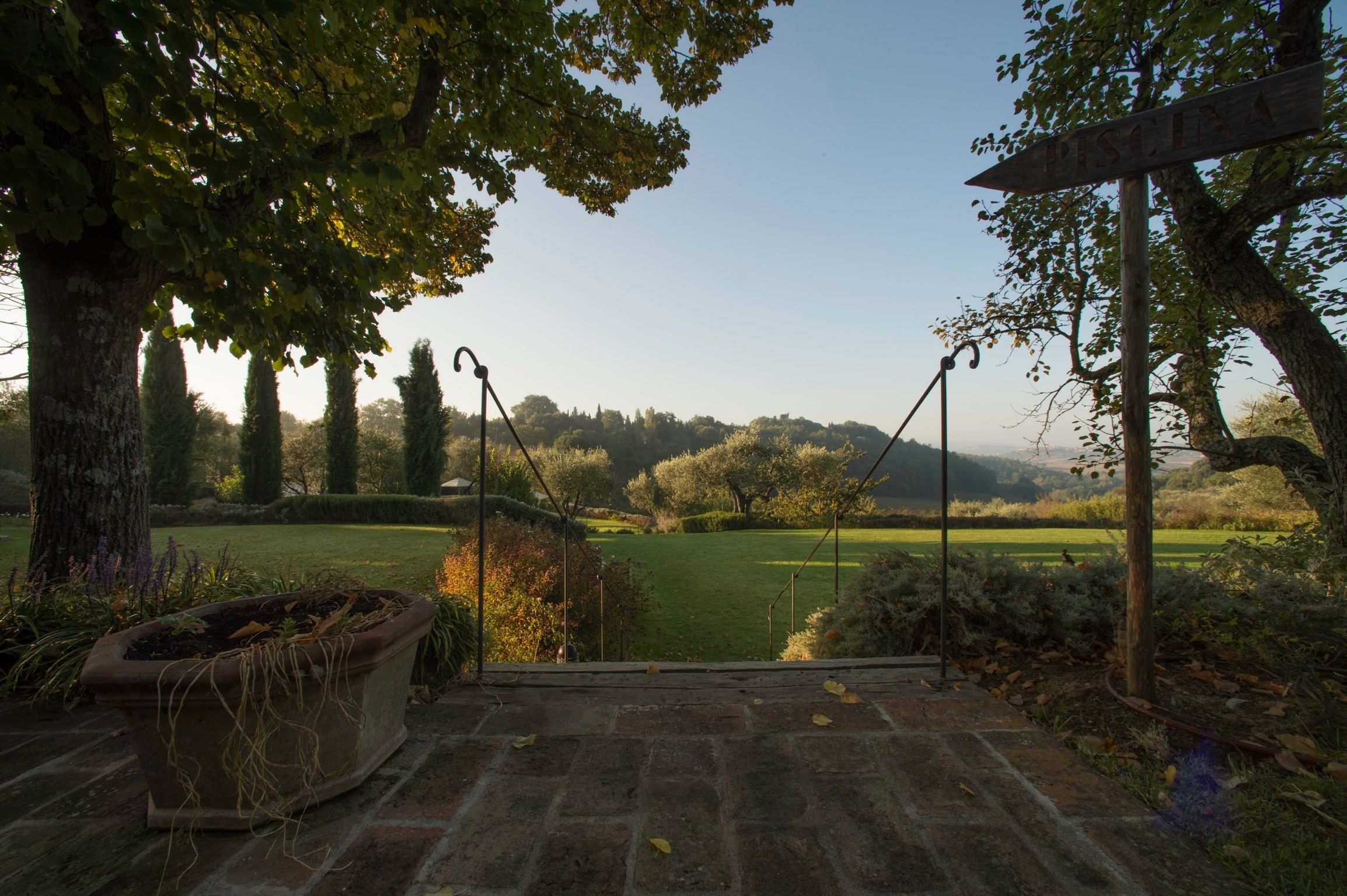 Un chemin de pierres mène à un point de vue donnant sur un jardin bien entretenu, agrémenté d’une pergola et d’un panneau indicateur.