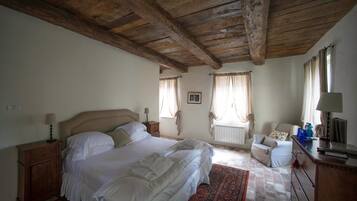 A bedroom with a large bed, wooden ceiling beams, a radiator, a chair, and a dresser.