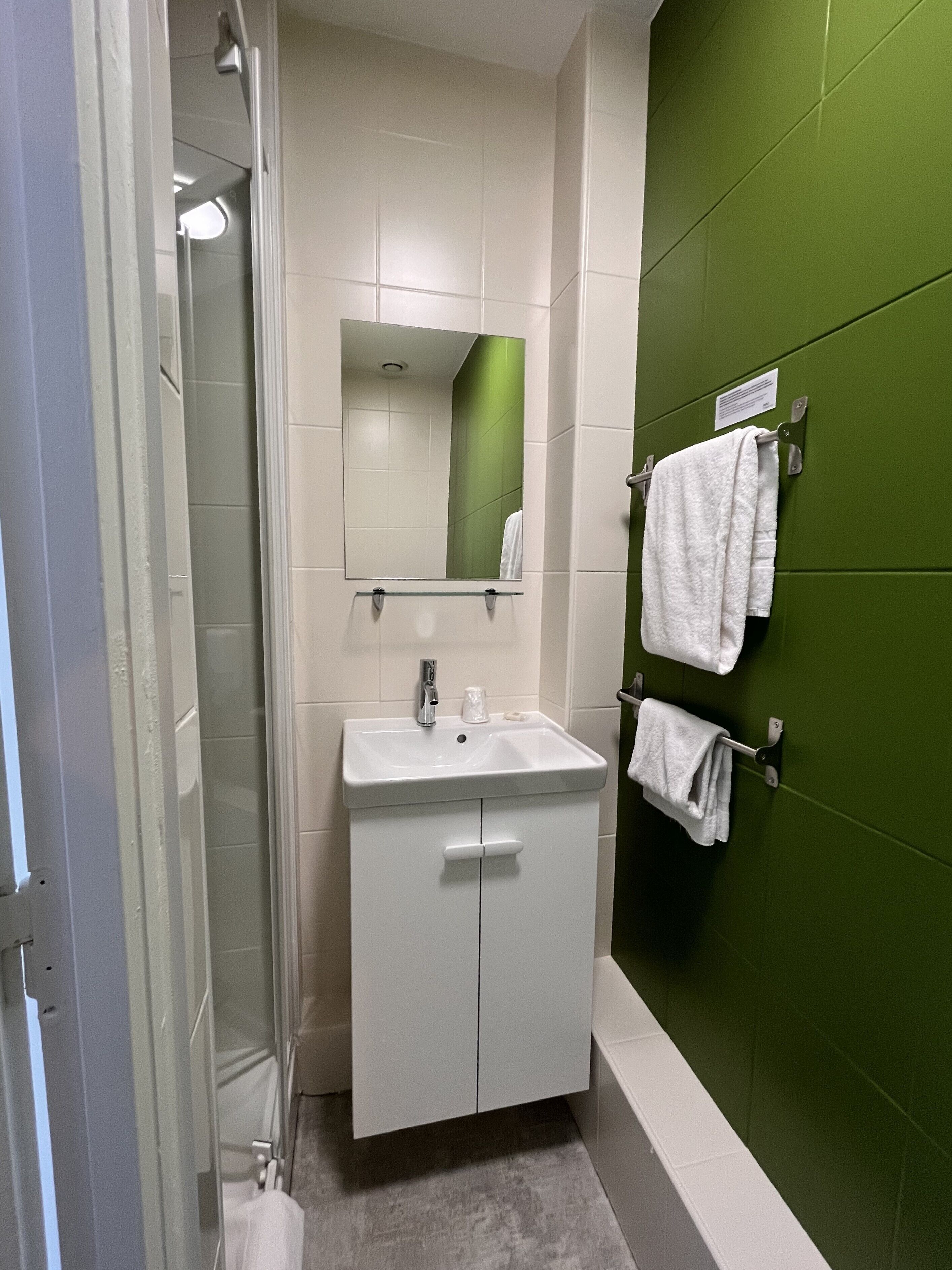 Un baño con un lavabo blanco, un espejo y una pared de acento verde.
