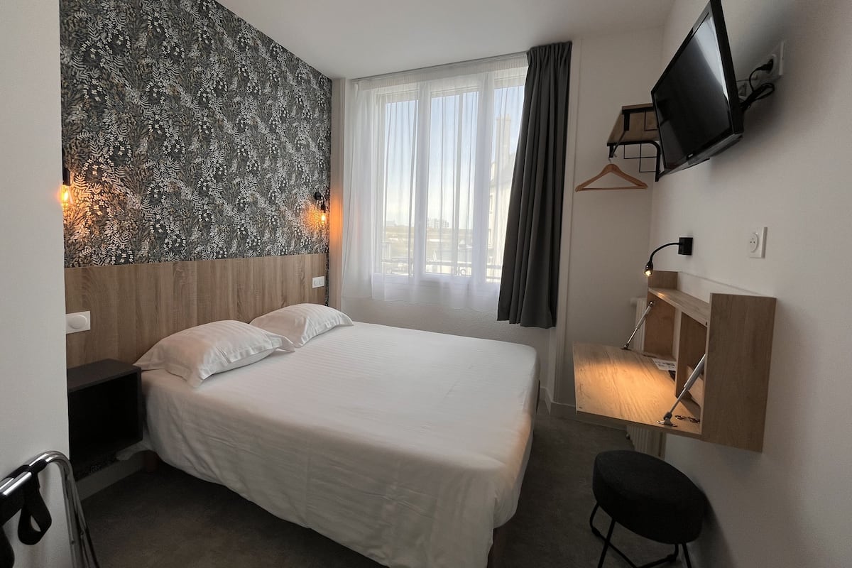Ein Hotelzimmer mit einem großen Bett, einem Schreibtisch mit Stuhl, einem an der Wand befestigten Fernseher und einem Fenster mit Vorhängen.