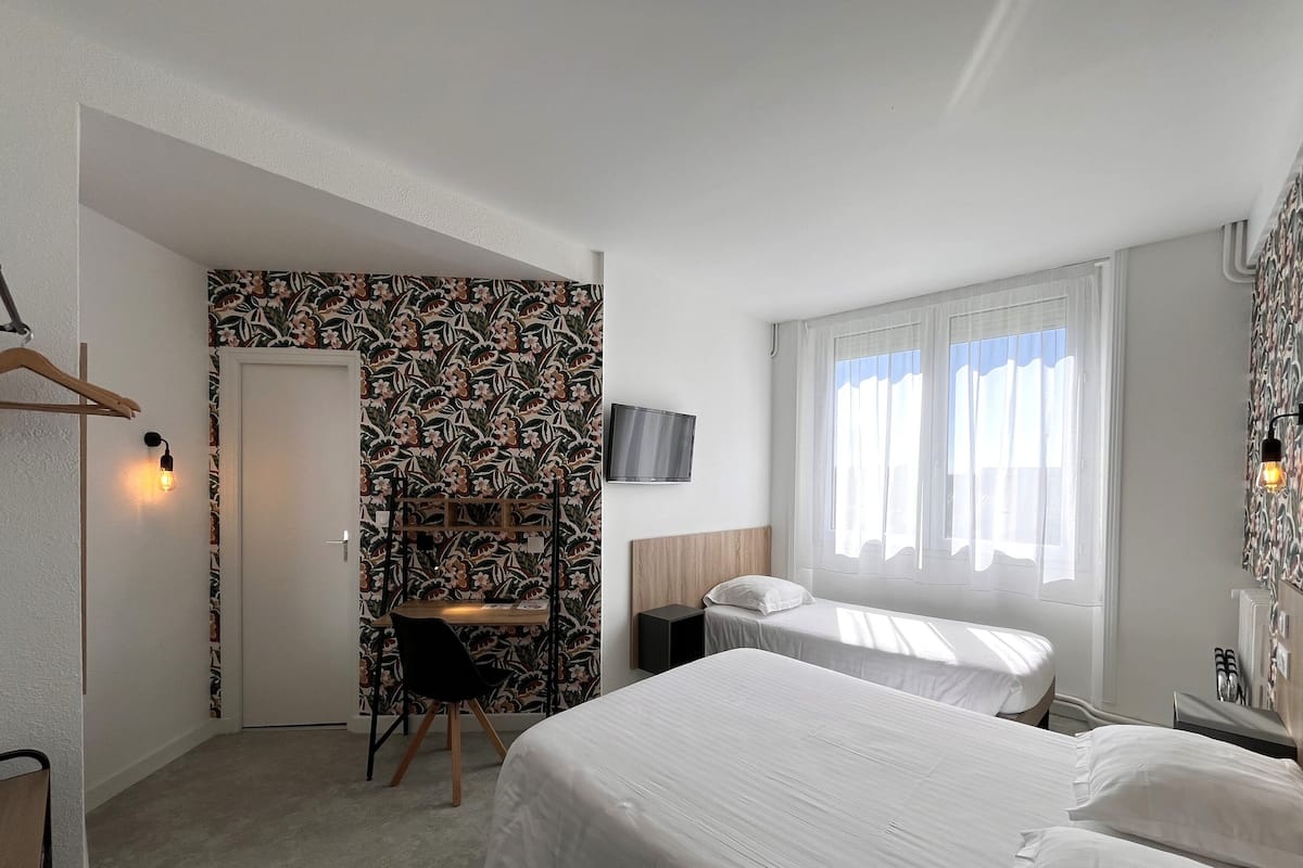 Ein Hotelzimmer mit Bett, Schreibtisch, Stuhl, Fernseher und einem Fenster mit Vorhängen.