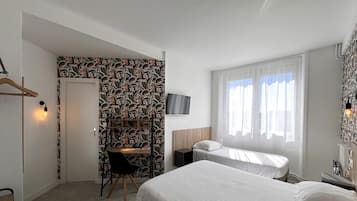 Une chambre d’hôtel avec un lit, un bureau, une chaise, une télévision et une fenêtre avec des rideaux.
