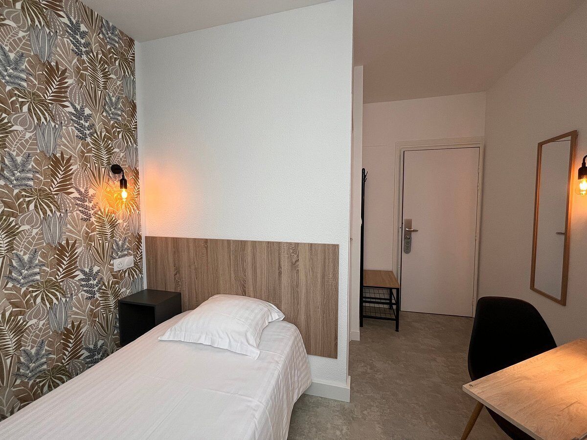 Habitación de hotel con una cama, un escritorio y una silla. Se ve una puerta que da a otra habitación.