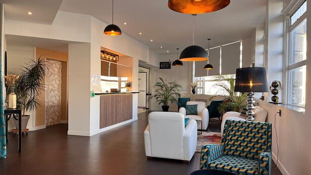 A spacious living area with a reception desk, white sofas, patterned armchairs, and pendant lighting. - Hotel Le Keroman (Lorient)