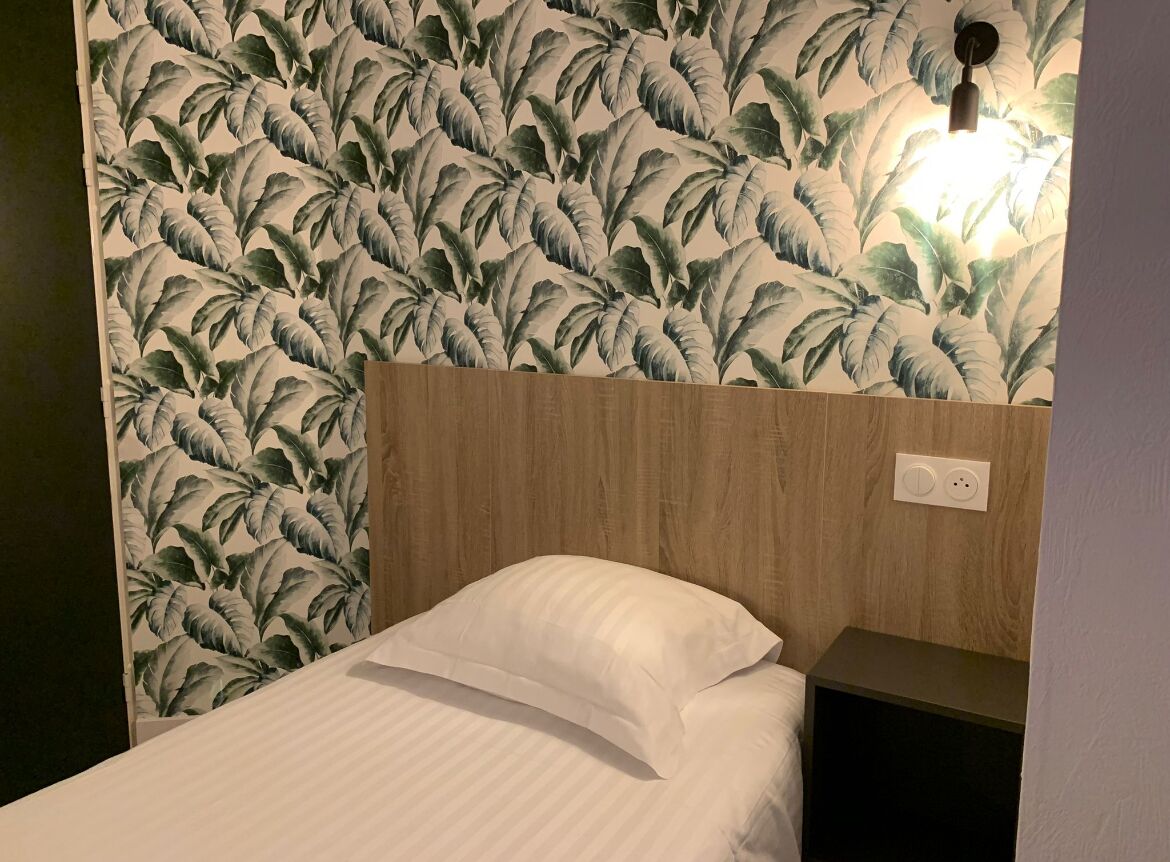 A hotel room with a bed, a wooden headboard, and a wall with a tropical leaf pattern.
