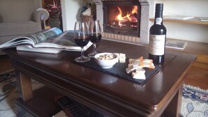 A cozy living room with a fireplace, a book, two wine glasses, a bowl of snacks, and a bottle of wine on a wooden table. - Hotel Rural Quinta do Silval (Alijó)