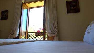 A bedroom with a bed, curtains, a window, and a balcony with flowers.