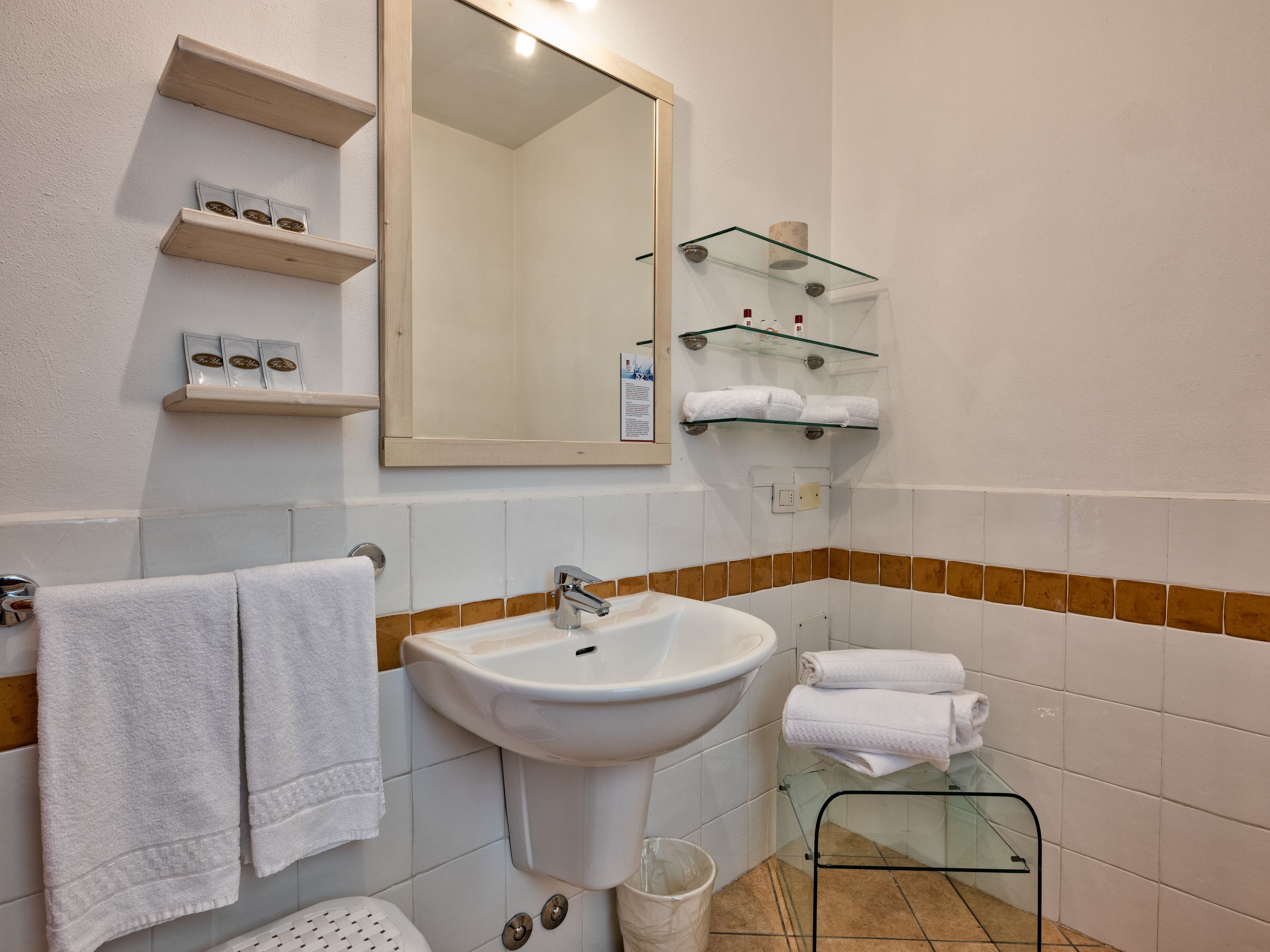 Une salle de bain équipée d’un lavabo, d’un miroir, d’un porte-serviettes et d’étagères en verre.
