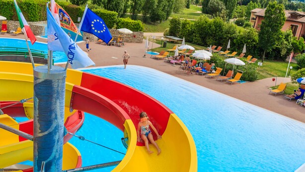 Un parque acuático con un tobogán de colores, una piscina y sillas de descanso.