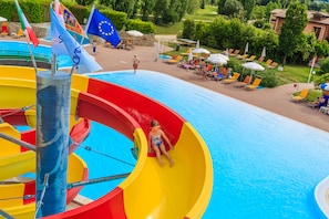 A water park with a colorful water slide, a pool, and lounge chairs. - Golf Residence (Castelnuovo del Garda)