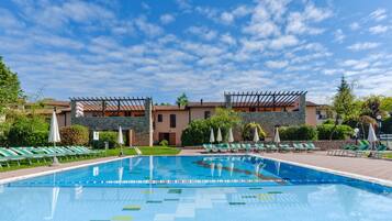 Una piscina con sillas de descanso y sombrillas, rodeada de edificios con fachadas de piedra y estuco.