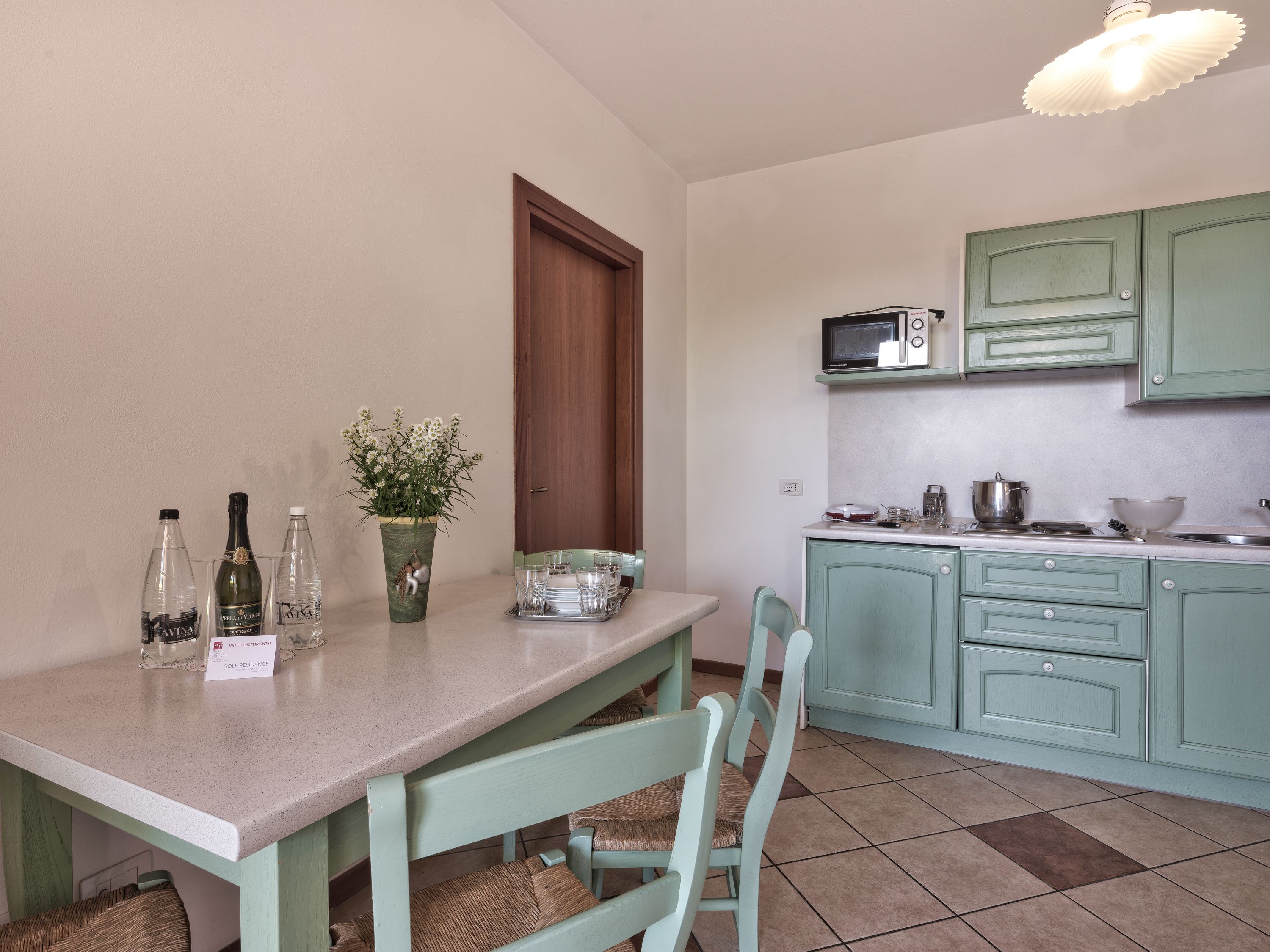 Una cucina con mobili color petrolio, un forno a microonde e un'area pranzo con sedie e tavolo.