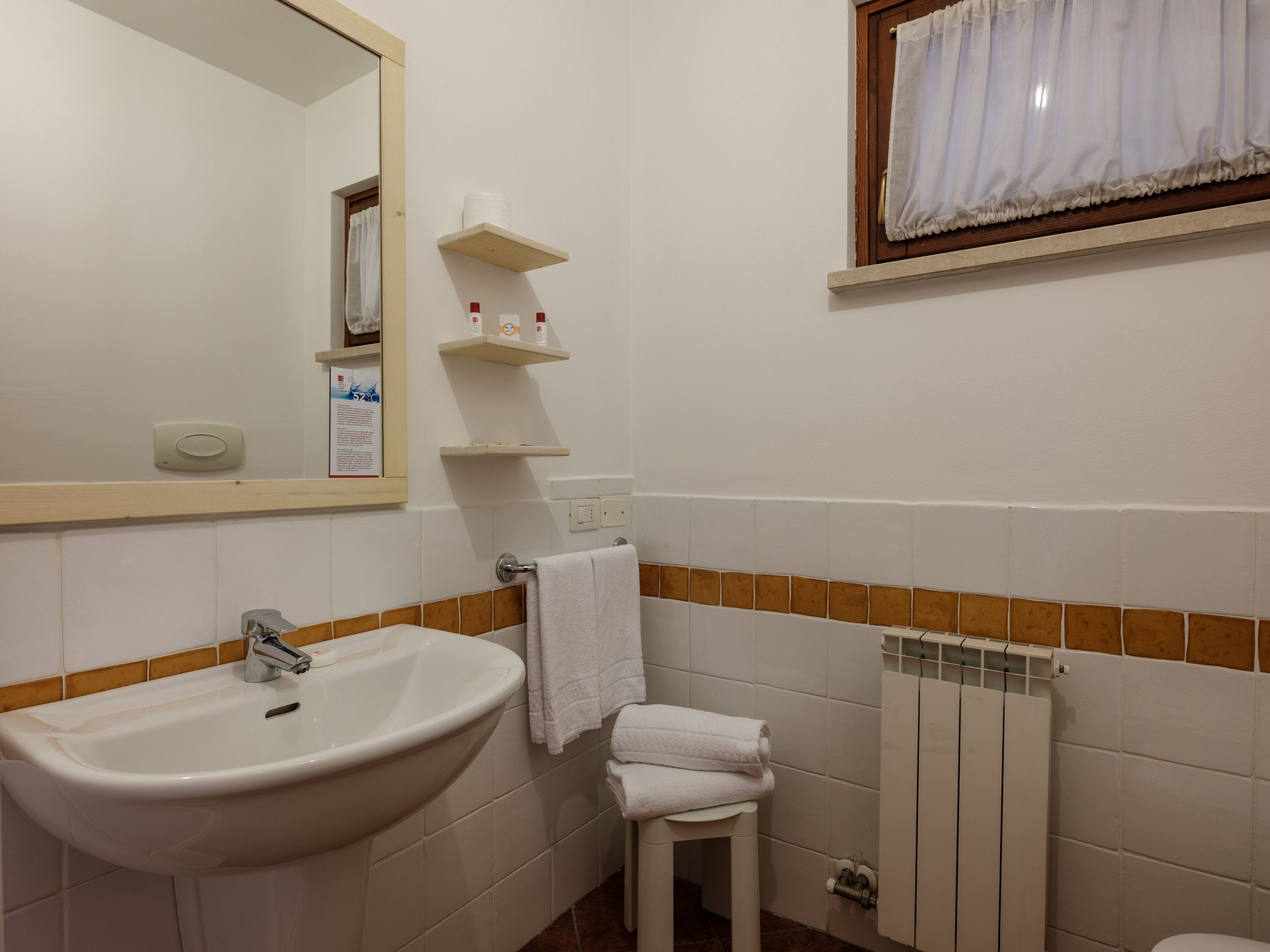 Ein Badezimmer mit Waschbecken, Spiegel, Handtuchhalter und einem Fenster mit Vorhängen.