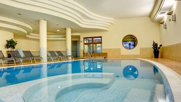 A modern indoor swimming pool with clear water, lounge chairs, and a unique ceiling design.