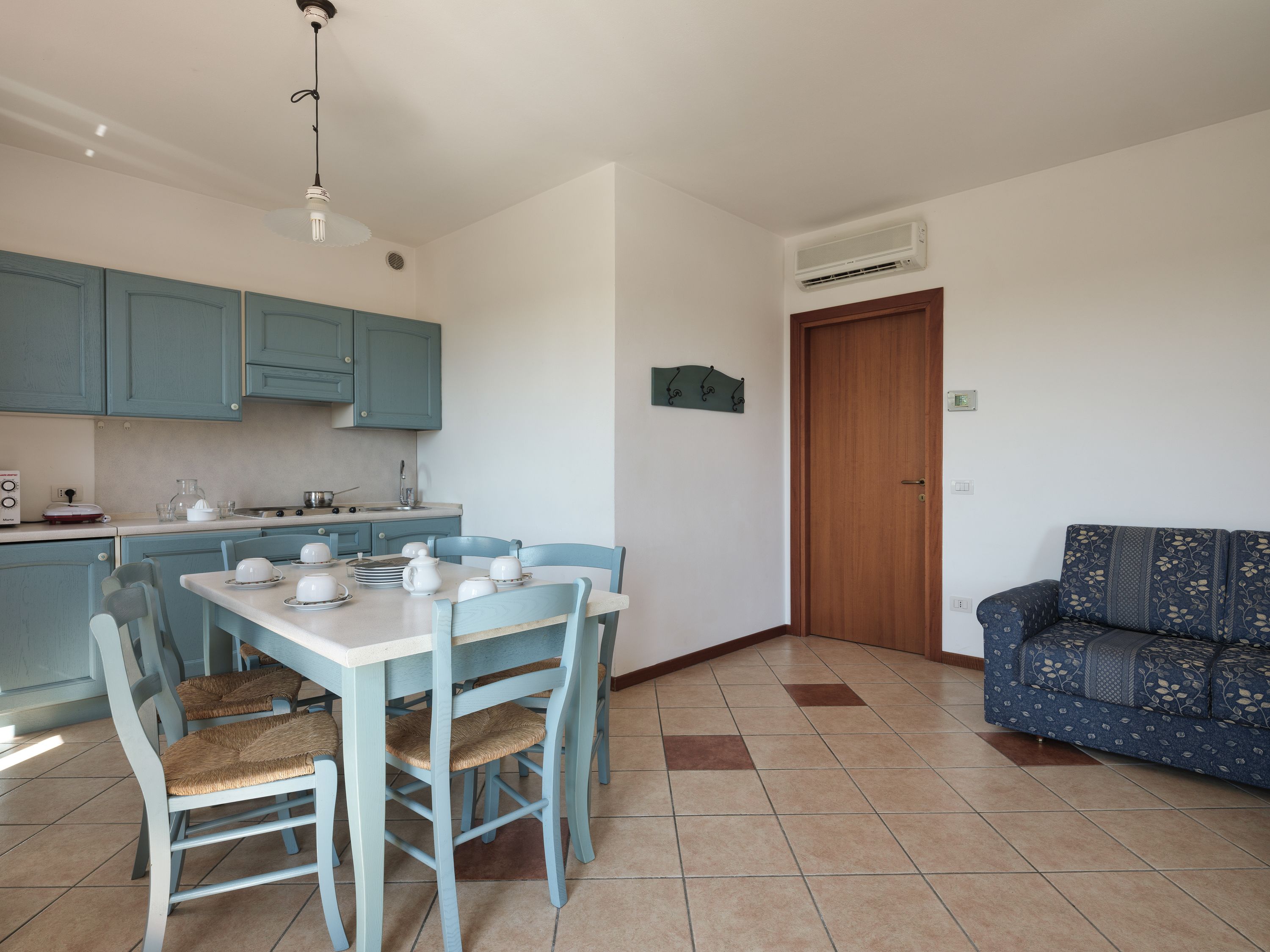 Cocina compacta con gabinetes color turquesa, una mesa de comedor con sillas y un sofá en la sala.
