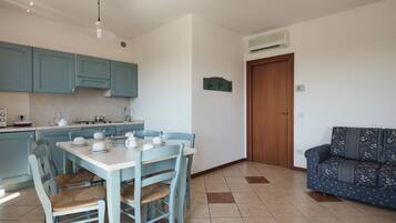 A compact kitchen with teal cabinets, a dining table with chairs, and a sofa in the living area.