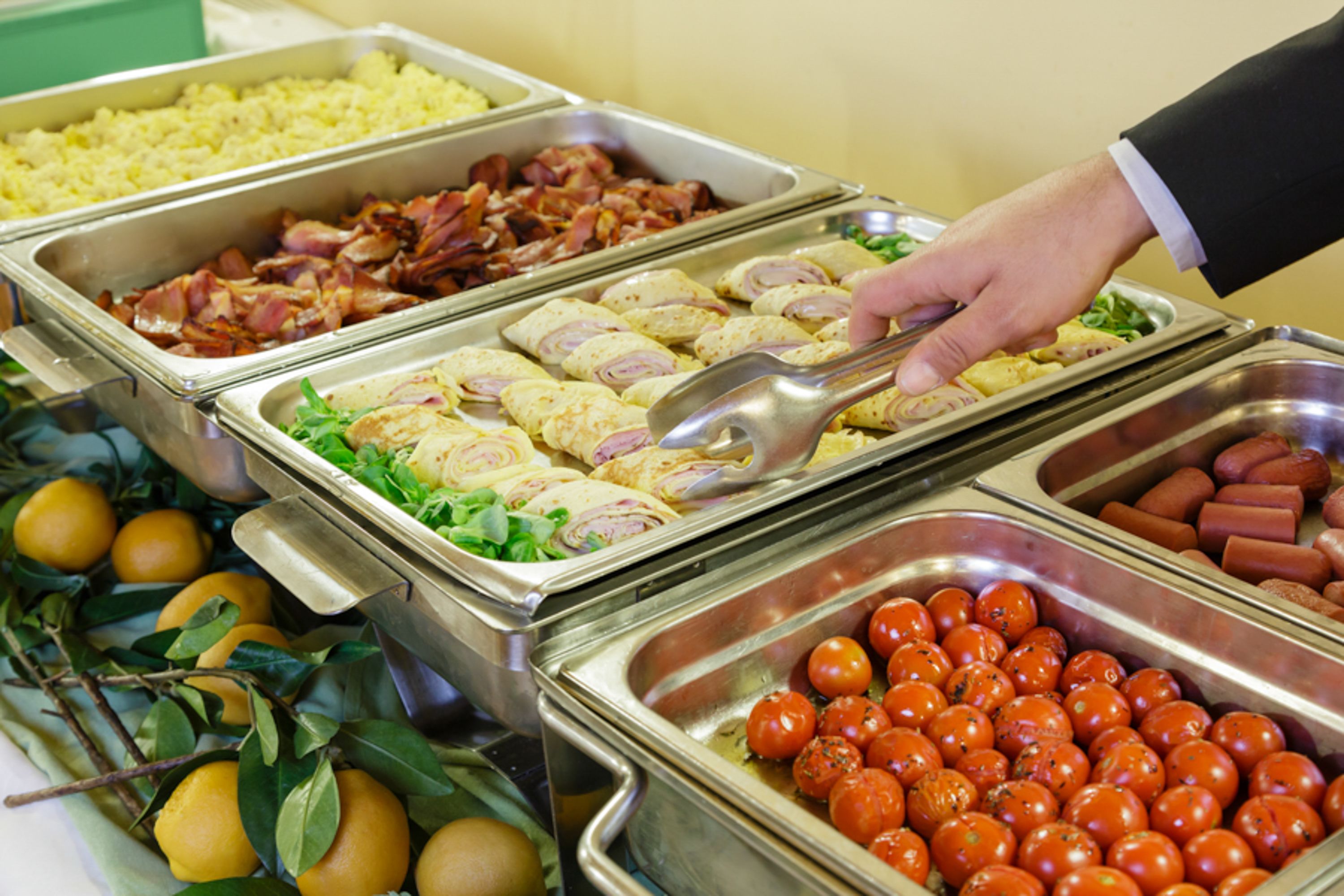 Een ontbijtbuffet met diverse gerechten, zoals spek, eieren en tomaten.