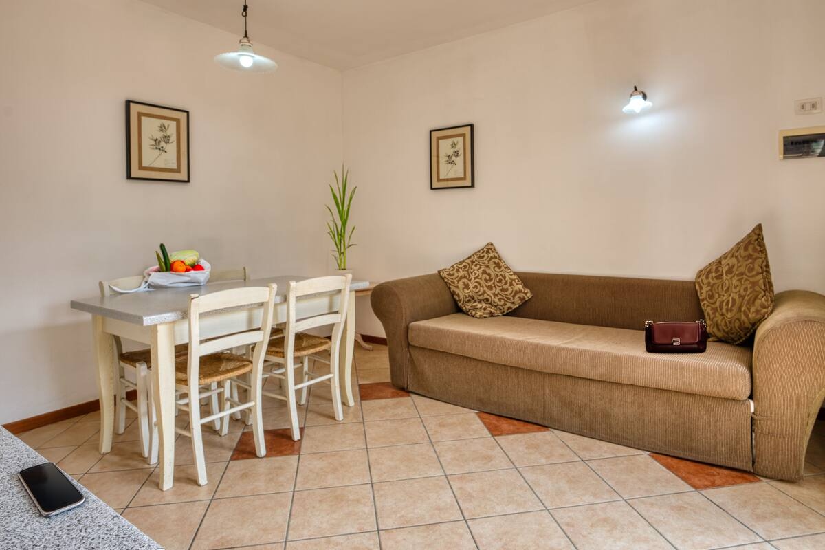 A living room with a dining table, chairs, a sofa, and a remote control on the floor.