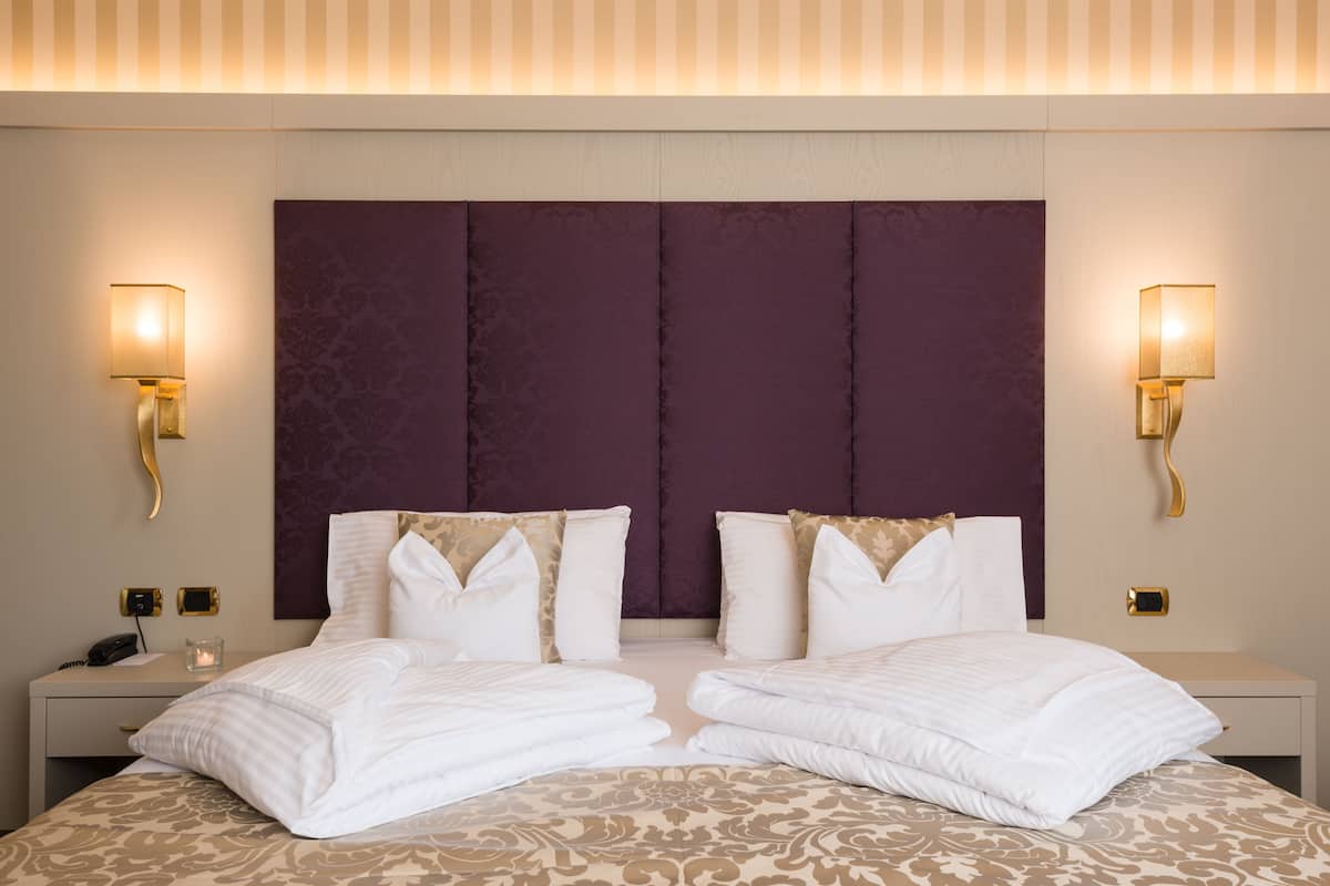 Una cama doble con cabecera, dos mesitas de noche y lámparas de pared.